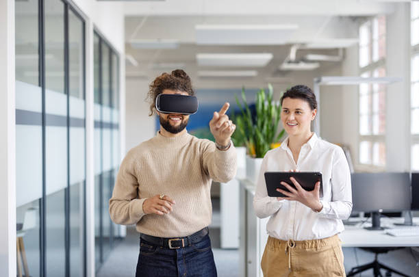 istock Happy businessman using VR glasses by colleague working on a digital tablet 1919234110