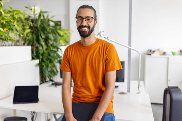 Portrait of a happy young middle eastern man sitting at his desk at startup office Portrait of a happy young middle eastern man sitting at his desk at startup office. Businessman at startup office looking at camera and smiling. north african ethnicity stock pictures, royalty-free photos & images