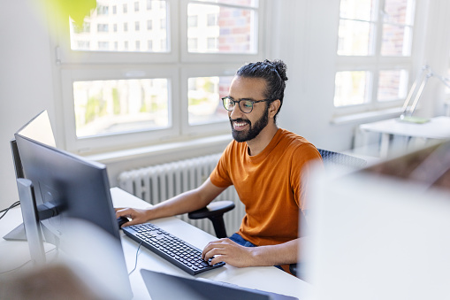 Happy young middle eastern man working on computer at office. Smiling businessman working on desktop computer at office.