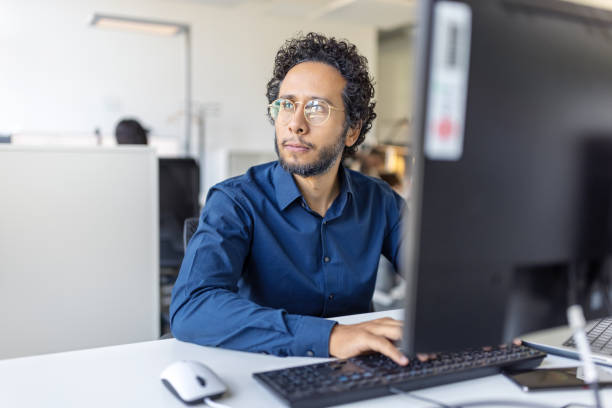 istock Confident young man sitting at desk with computer looking away and thinking 1919240546