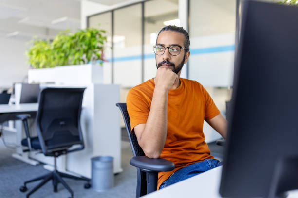 istock Young man sitting at desk looking away and thinking 1919242166
