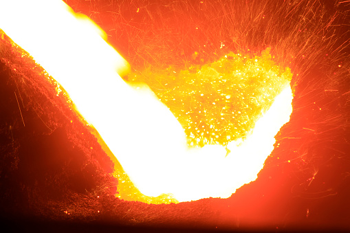 flowing molten iron in the iron works blast furnace taphole, closeup of photo