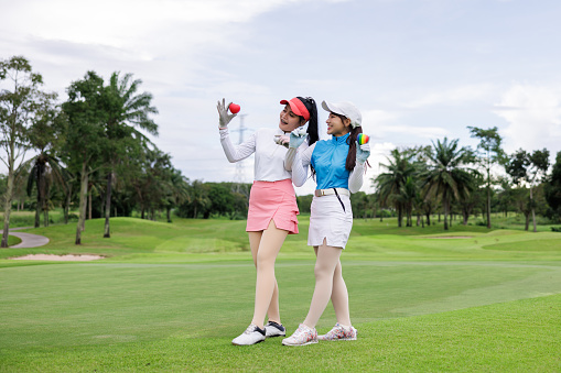 Portrait of two young asian female profestional golfer holding red heart at the course over white sky background,
