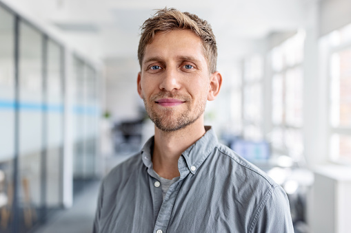 Close-up portrait of businessman looking at camera while standing in office. Confident male business executive at coworking office space.