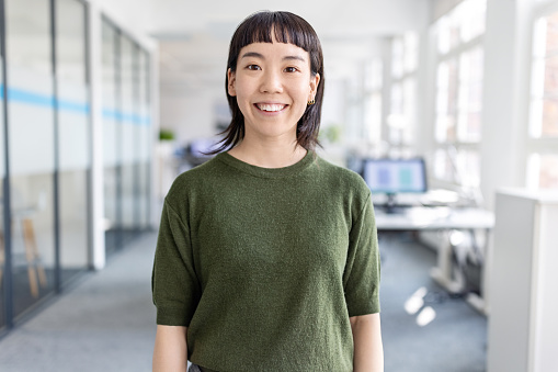 Portrait of cheerful young asian businesswoman standing in office. Japanese female entrepreneur looking at camera at startup.