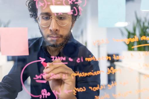 Middle eastern businessman writing on transparent wipe board in office during brainstorming session. Startup entrepreneur working on new strategy for the project in office.