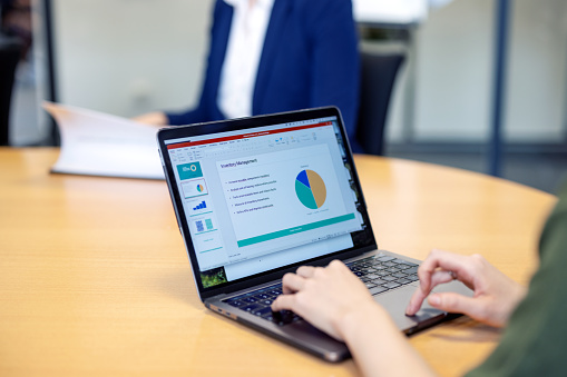 Close-up of a woman preparing business report on a laptop sitting at office. Female working on laptop with statistical presentation on seen on screen.