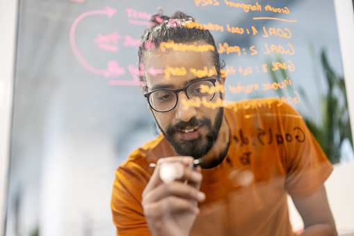 Middle adult businessman writing ideas on transparent wipe board in office. Startup business entrepreneur working on new strategy for the project in office.