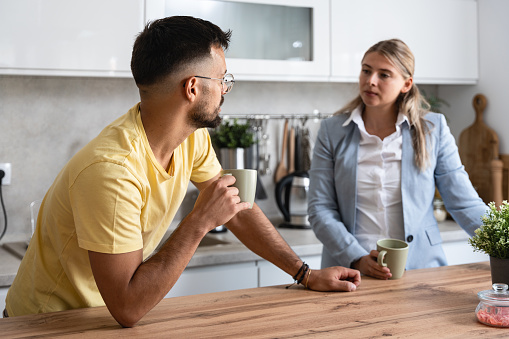 Business colleagues talk during lunch break in office kitchen. Woman communicates with workmate hold coffee cups enjoy conversation, discuss work or personal. Good relations at work concept