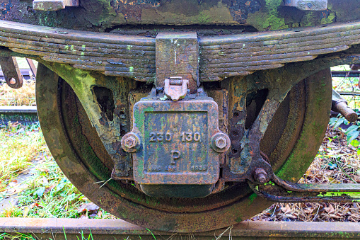 Close-up of very old damaged, worn and rusty railway disc wheels with frame, bracket, axle bearing and brake, disused tracks at old train station