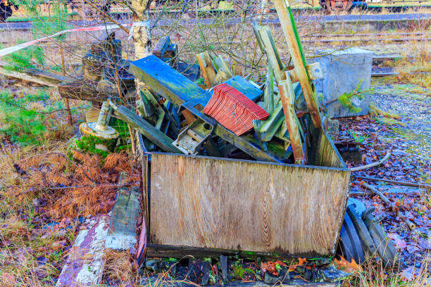 Metal pieces and bars stacked in wooden container in backyard of an old disused train station, wild bare vegetation, accumulated industrial garbage