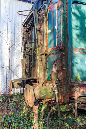 Side view of connecting buffers and fallen door of a dilapidated, rusty, damaged and abandoned train carriage, peeling paint, disused tracks at former As railway station, Limburg, Belgium