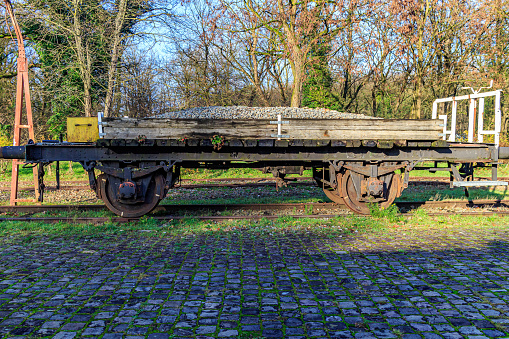 Old platform wagon with gravel between wooden planks on disused tracks at former As train station, bare trees in background, sunny autumn day in Limburg, Belgium