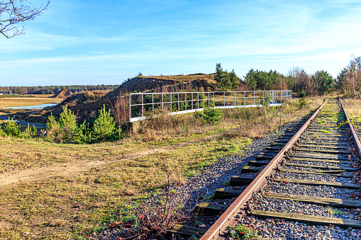 Train tracks crossing a bridge with bare trees and wild vegetation in background, autumn landscape against blue sky, sunny day in Hoge Kempen national park, As Limburg, Belgium