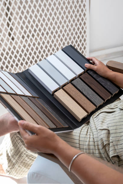 Interior designer hand holding sample book with stack of vinyl wood sheet to select floor baseboard or plinth, tile material works