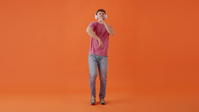 Cheerful man using headset and dancing in orange studio