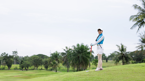 Portrait of young asian female golfer holding the golf club at the course over white background,