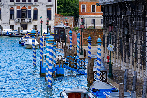 Idyllic view of the old town of Italian City of Venice with moored boats and blue and white striped poles at pier on a cloudy summer day. Photo taken August 6th, 2023, Venice, Italy.