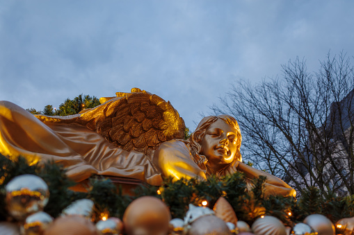 Bonn, Germany - Dec 6, 2023: Golden angel figurine amidst festive decorations with a blurred background of trees and twilight sky.