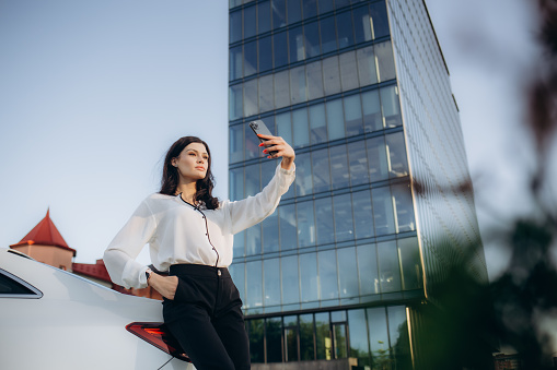 Beautiful business lady takes a selfie on the phone near the car