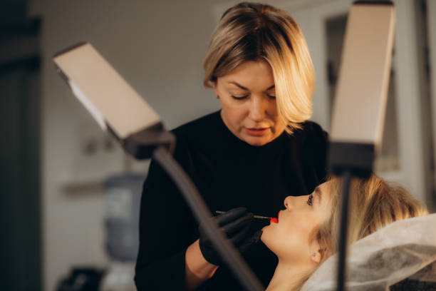 istock Face of girl in profile during microblading permanent makeup process. Hands of tattoo master holding professional ink machine with medicine needle 1919400305
