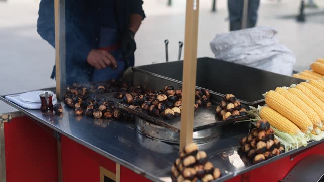Trukish man with street wagon sells roasted chestnuts and boiled fragrant corn to tourists