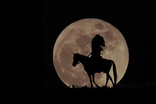 Silhouette of indians man riding a horse on full moon background