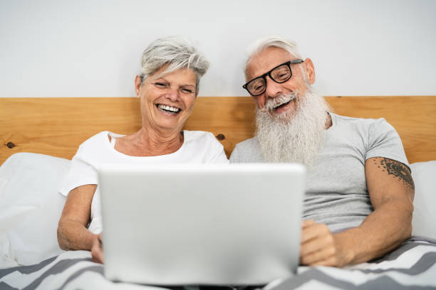 istock Happy senior couple having fun using laptop while being in bed under blankets - Technology and elderly people lifestyle concept 1919408770