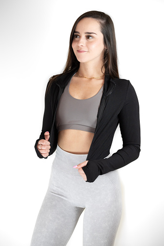 An attractive young woman wearing a black jacket and gray pants, smiling and posing for the camera in a relaxed and confident stance