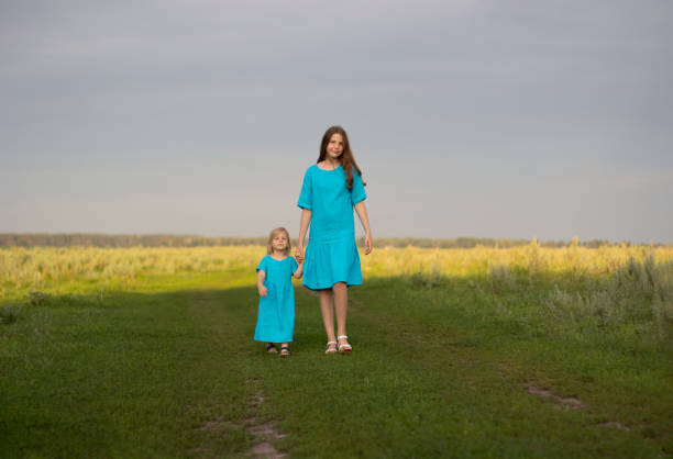 Two sisters in blue linen dress have fun in the park with blooming lilacs, enjoy spring and warmth. Beautiful spring garden. Happy childhood. Family, love, peace and happiness concept