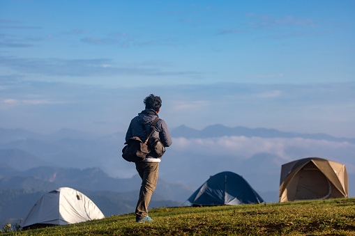 Traveller is trekking to the mountain top at the campsite with several tents among the beautiful scenic of high altitude view for outdoor adventure vacation travel