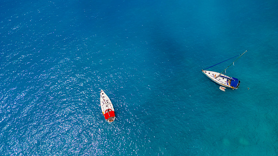 Two sailboats anchored in a beautiful bay of Porto Katsiki, Lefkada, Greece. The sea is blue and sun is reflecting on the surface.