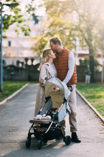 Stroller Serenity in the Park Embrace the peaceful ambiance of a family stroll in the park, where a mother and father leisurely walk, pushing their baby in a stroller, creating a harmonious and idyllic scene. three way kiss stock pictures, royalty-free photos & images