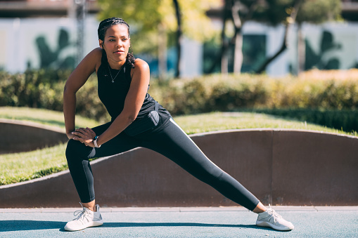 Feel the energy as an African-American woman indulges in invigorating stretches, preparing her body for a spirited run in the park â a dynamic image of vitality and wellness.