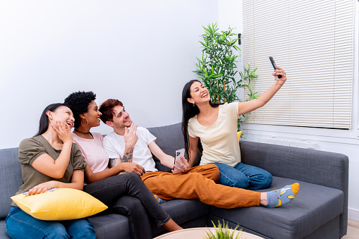 Joyful friends taking a group selfie on a sofa in a bright living room.