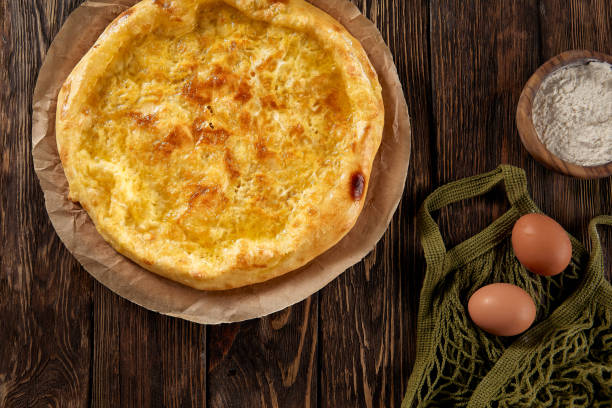 istock Golden-browned Megrelian khachapuri on parchment, with a rustic wooden backdrop, inviting and traditional 1919496395
