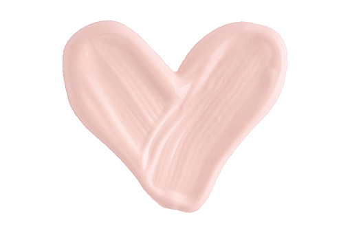 A smear of foundation cream or concealer in the shape of a heart isolated on white background, macro. Texture of cosmetic liquid foundation or beige cream smudge, smear, stroke.