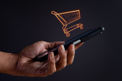 Hand holding smartphone with shopping trolley icon. Online shopping, business concept.