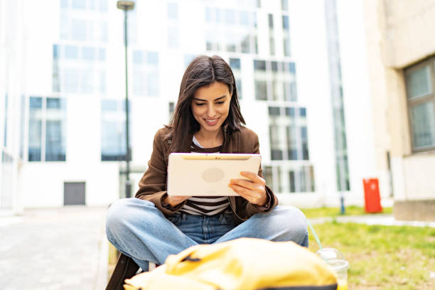 istock Female university student sitting on bench in campus using digital tablet 1919520370