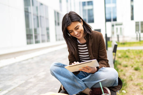 istock Female university student sitting on bench in campus using digital tablet 1919520896