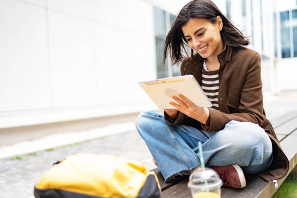 istock Female university student sitting on bench in campus using digital tablet 1919523169