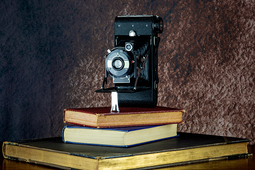 Vintage folding film camera on a pile of old books on a wooden shelf