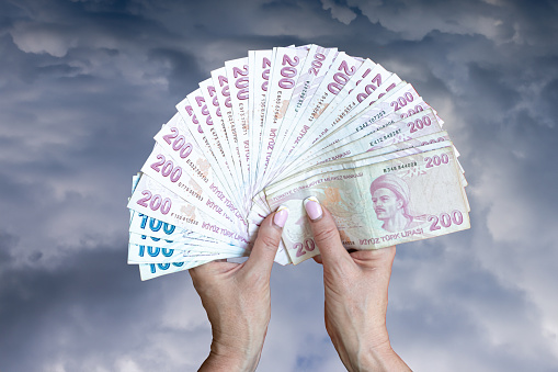Close-up of female hands holding Turkish lira banknotes on a blue-gray background. Money.