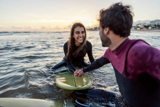 istock Surfers sitting on surfboard in water and holding hands. 1919555441