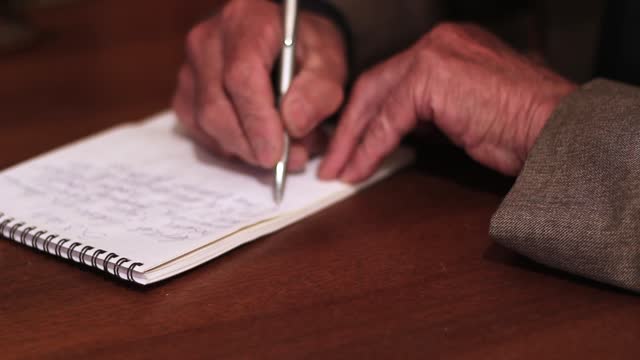 Senior Man Writing On A Notepad At Home