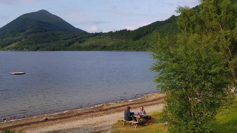 Aerial view of Woman and Man Admiring Picnic by Lake with Summer Mountain View