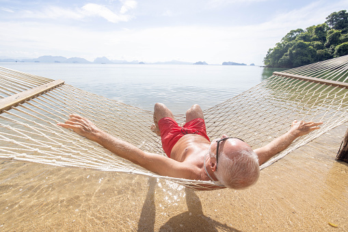 Male senior relaxing while on vacation in Asia, he enjoys the sea, sun and hammock.