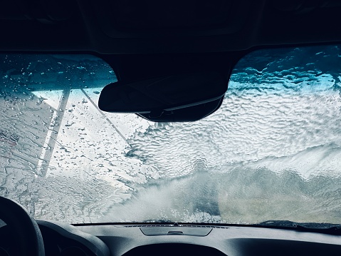 Man splash soapy water for wash car by high pressure water jet at the quick car cleaning station service - view from inside the car to the front windshield