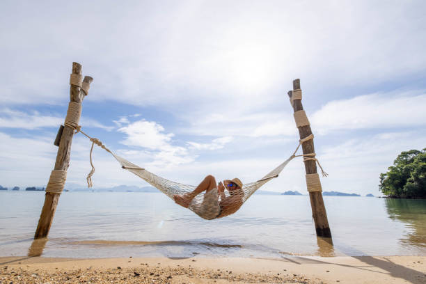 istock Man relaxing on hammock by the beach, he uses his mobile phone 1919598937