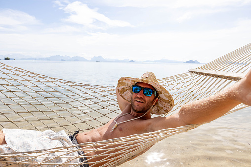 30's man relaxing on hammock over sea in Thailand, Southeast Asia vacations.